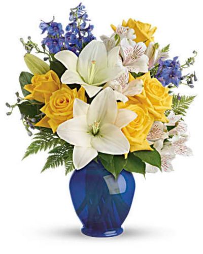 Like a sunny day at the shore, this bright bouquet invigorates and inspires! Radiant yellow roses, white lilies and blue delphinium are expertly arranged in our bold blue plastic ginger jar.
Sunny yellow roses, white asiatic lilies, white alstroemeria, and blue delphinium are arranged with leatherleaf fern and lemon leaf.